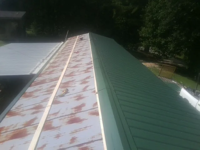 Old rusted panels beside newly installed green metal roofing — Wind Damage Roof Repair by Roofing Brothers in Diamondhead