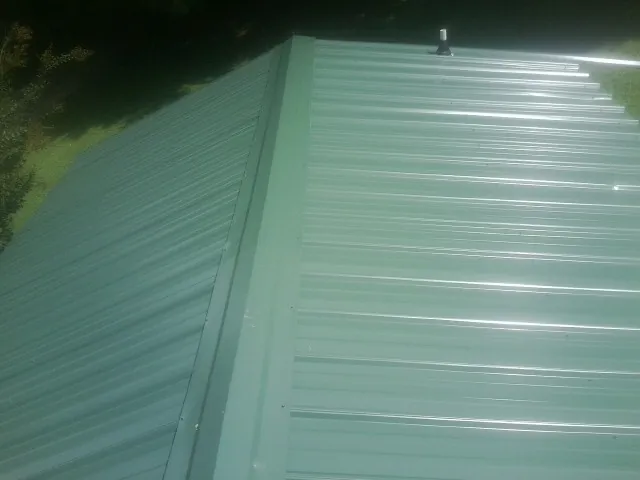 New green metal panels meeting at the ridge of a roof — Flat Roof Repair work by our crew in Diamondhead