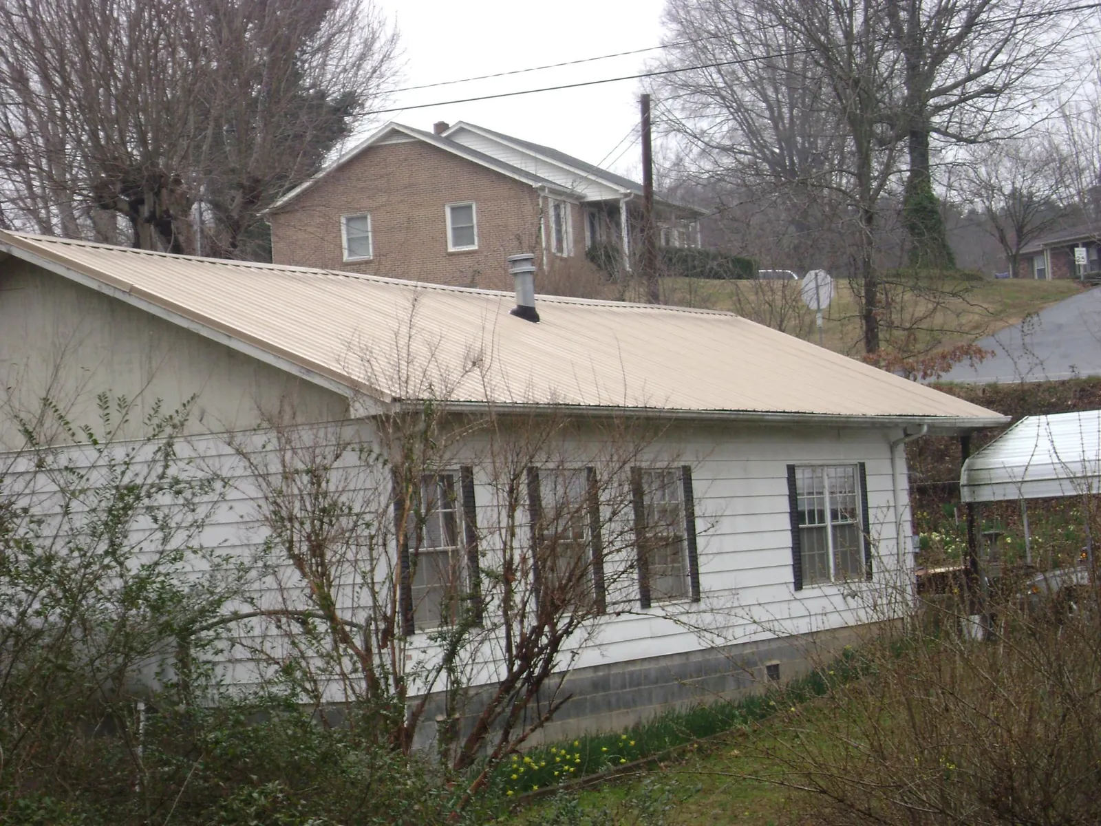 Tan metal roof on a white sided house set into a hillside — Commercial Roofing by Roofing Brothers in Diamondhead
