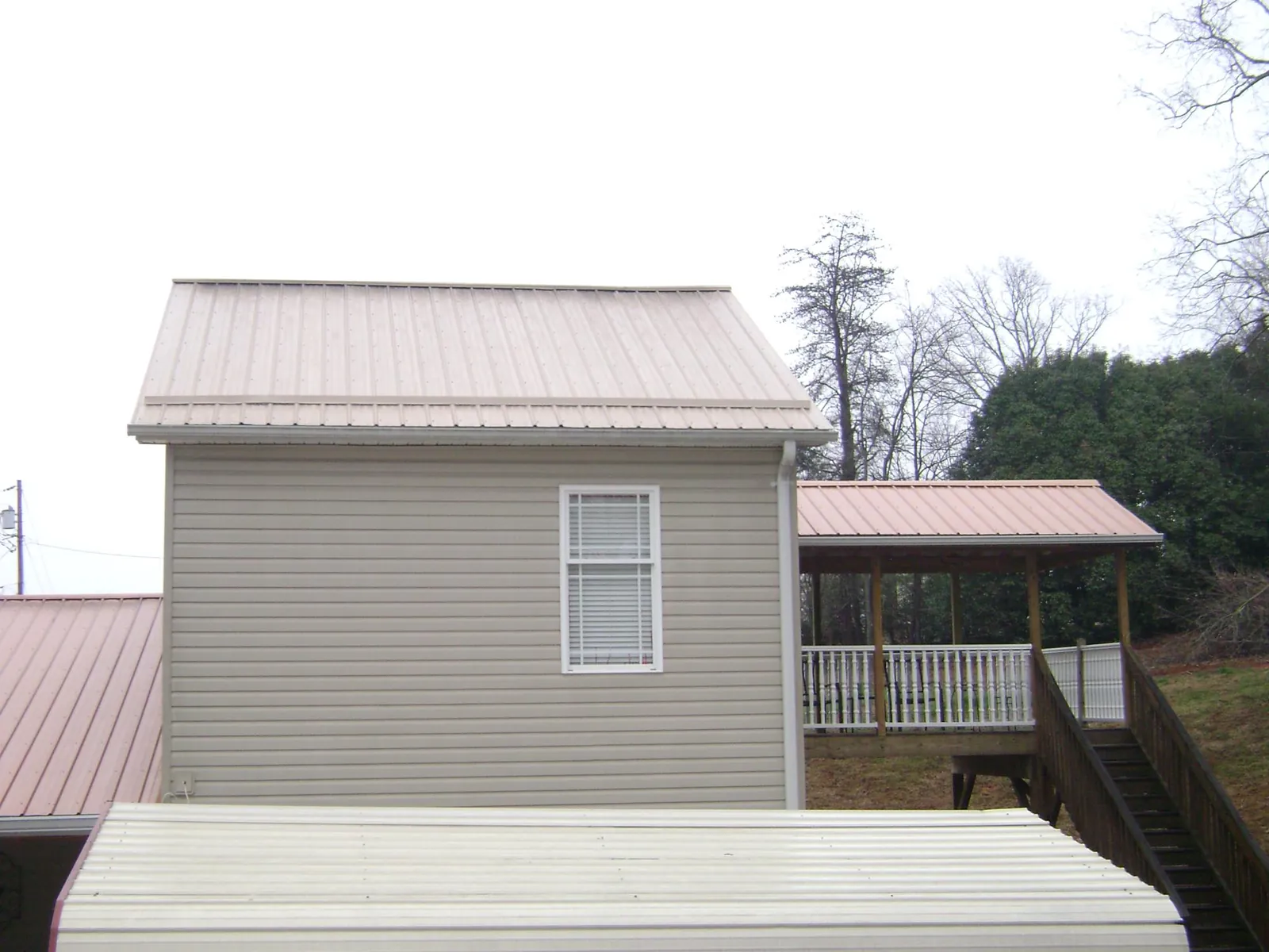 Tan metal roofs on a two story addition and attached porch, from a Roof Replacement job in Diamondhead